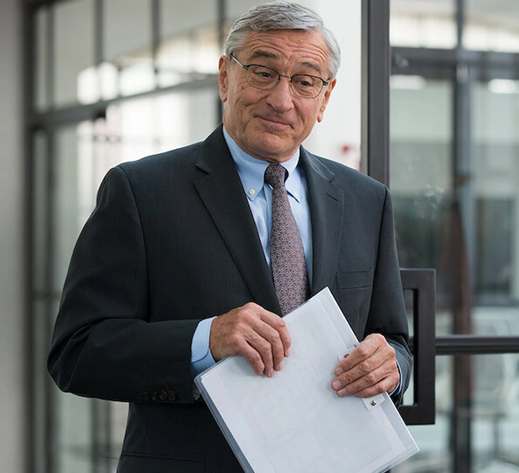 Robert De Niro as Ben in The Intern, holding a folder of papers.